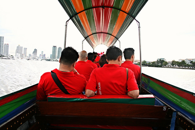 Curating Onboard Activities Corporate team in red shirts traveling by traditional long-tail boat in Bangkok.