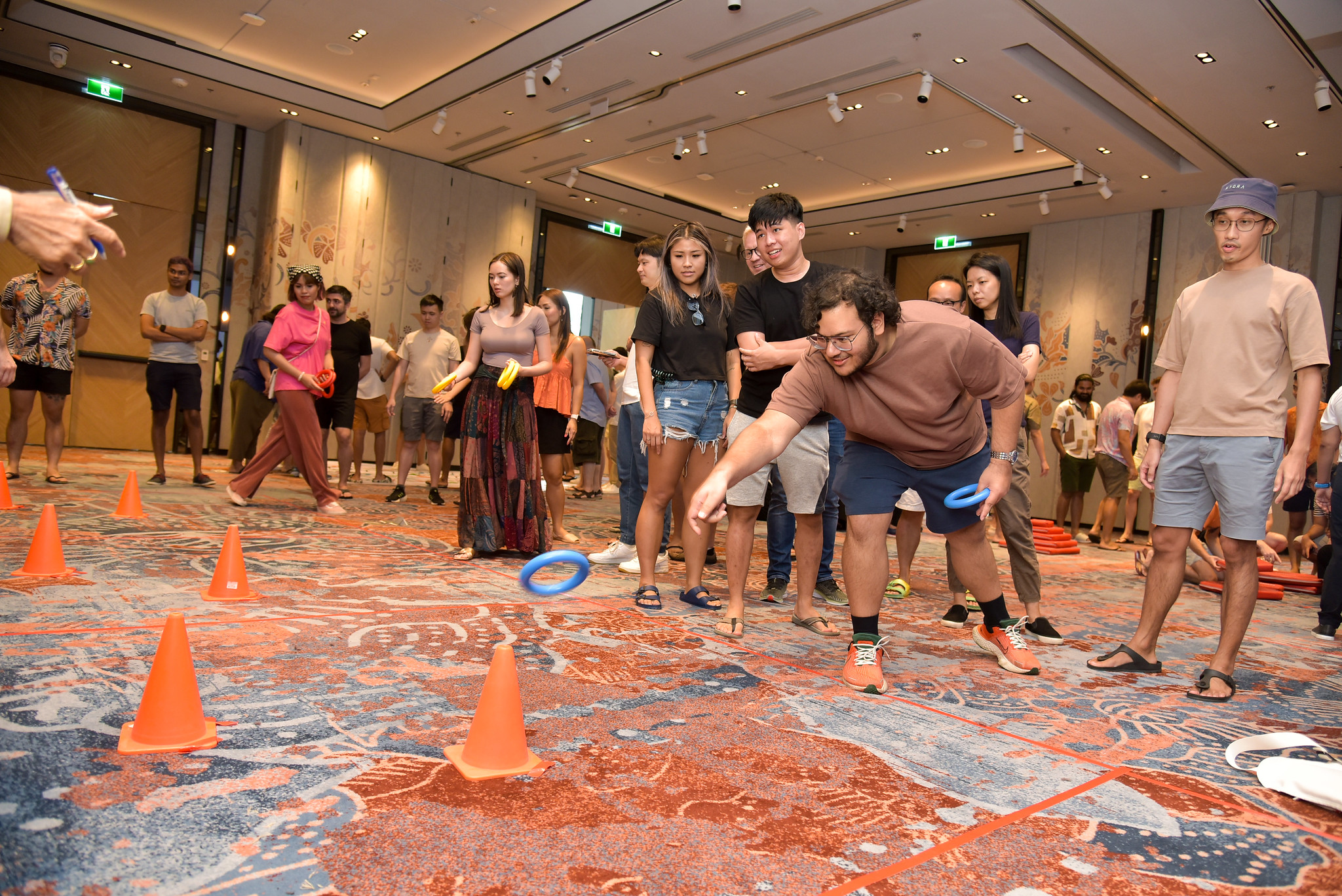Accuracy Coordination Games Participants in a large indoor hall compete in a ring-toss game, aiming at targets placed among orange cones during a coordination and accuracy challenge.