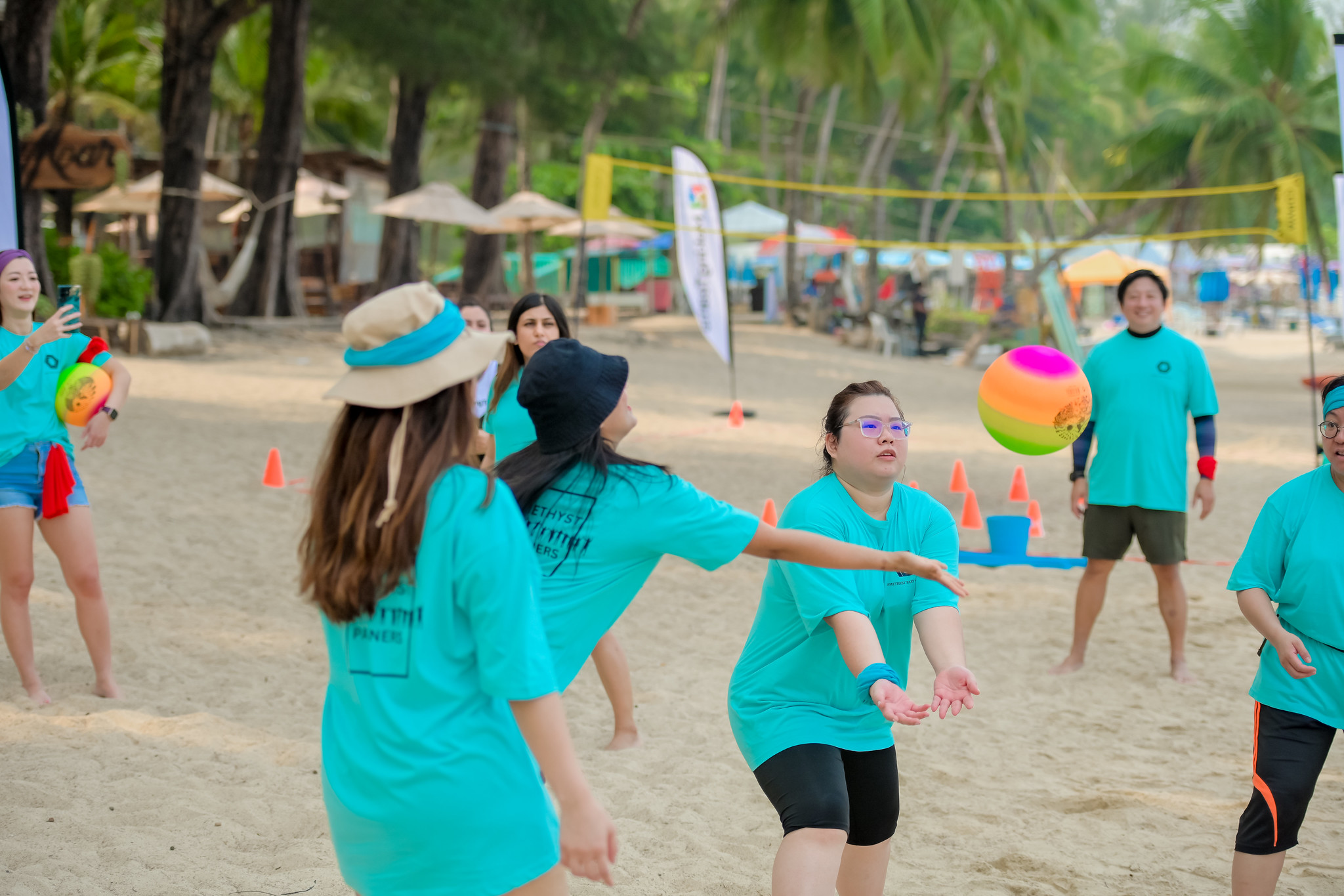Nature as a Team Catalyst A group of participants in turquoise shirts takes part in beach games under palm trees in Phuket, focusing on teamwork as they toss a colorful beach ball.