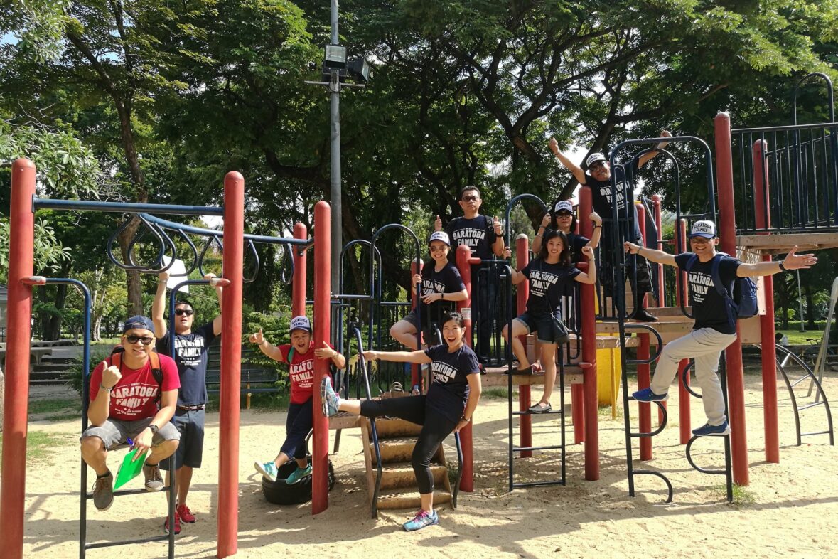 A corporate team posing and playing together on an outdoor playground structure in Bangkok.