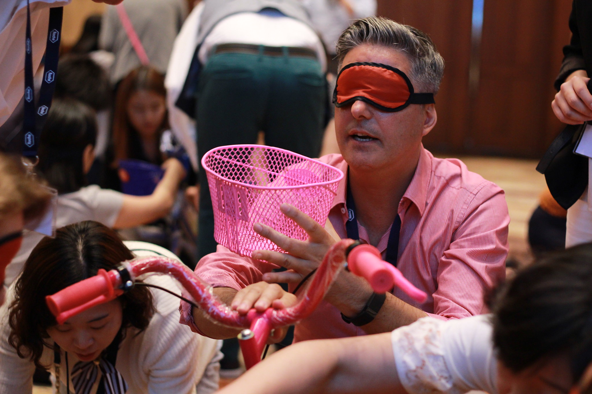 The Social Impact Moment Participant wearing a blindfold assembles a bicycle component with team support during a social impact team-building exercise.