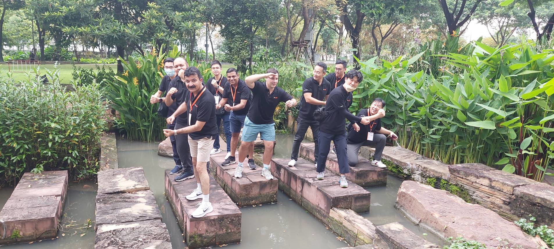 Corporate team participating in an outdoor experiential learning challenge, balancing on stone platforms in a park setting.