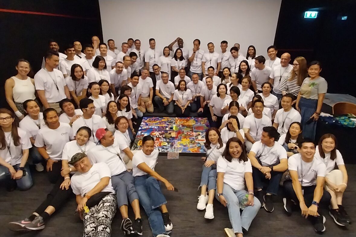 Large corporate team participating in an art-based team building workshop, posing together with expressive gestures on a stage.